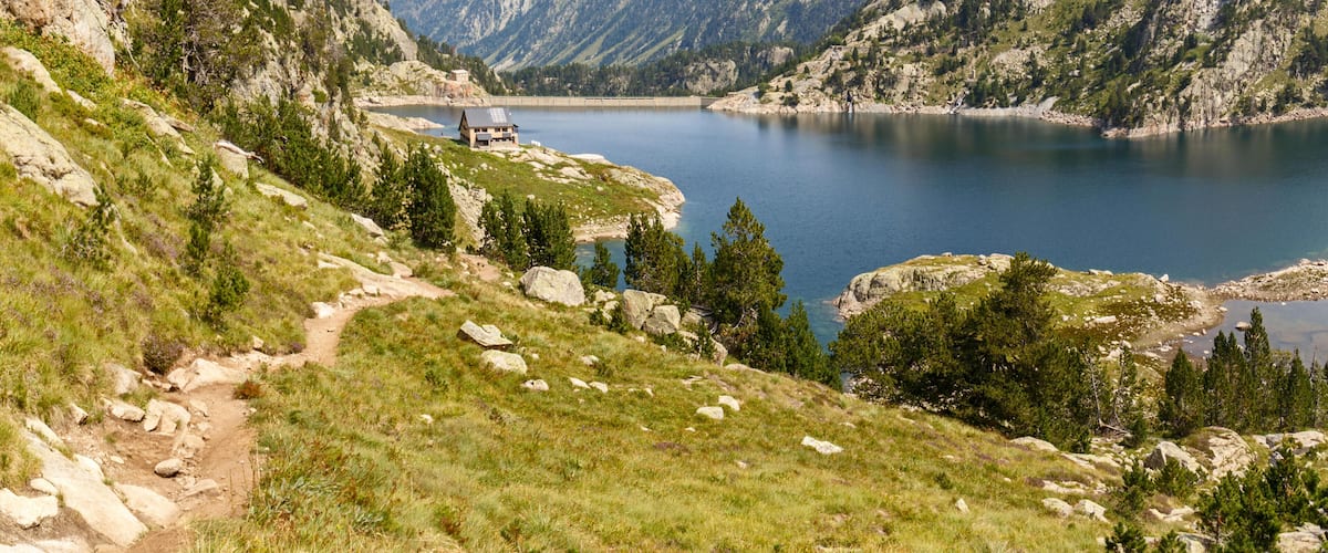 A mountainous landscape with a lake, a small building, and a path.