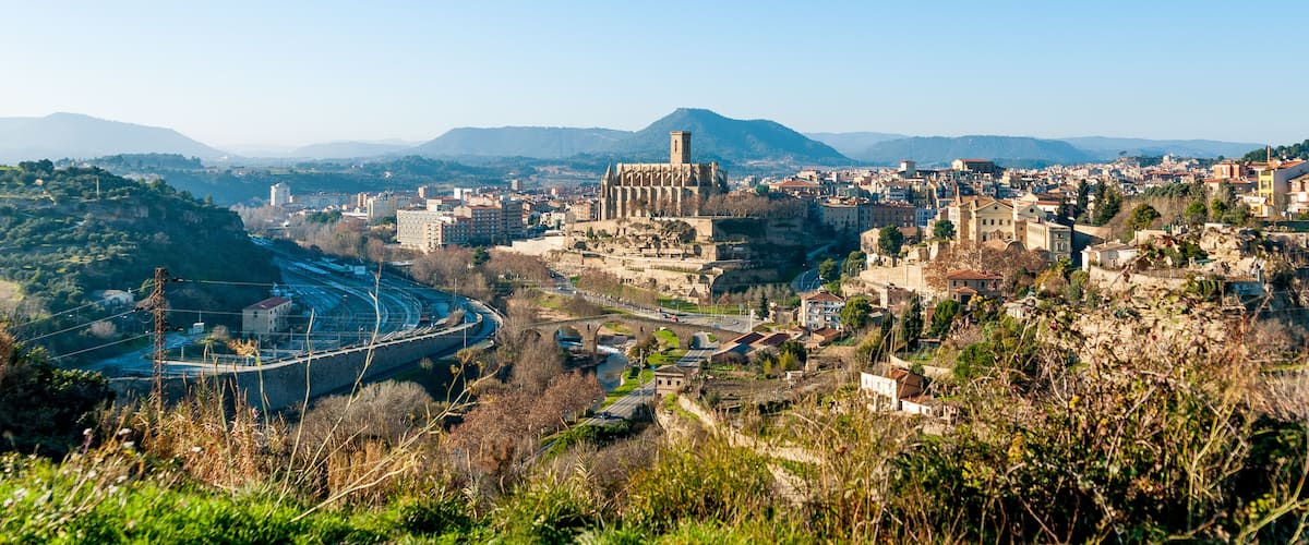 A cityscape with a prominent cathedral, a winding road, and surrounding hills.