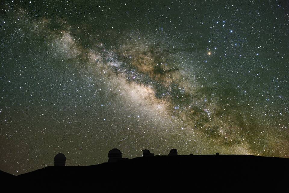 A starry night sky with the Milky Way visible, silhouettes of a dome and a telescope, and a person observing.