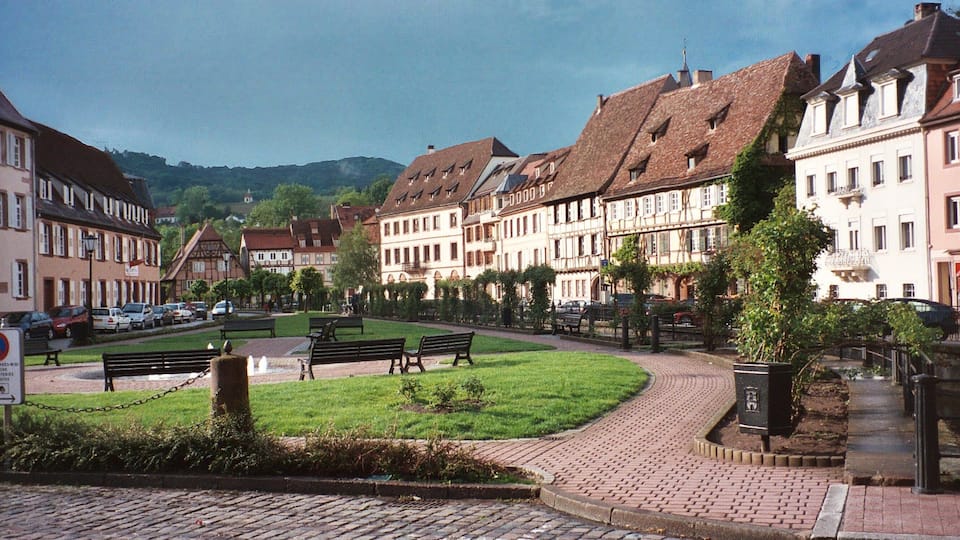 A cobblestone square with benches, surrounded by historic buildings with steep roofs.