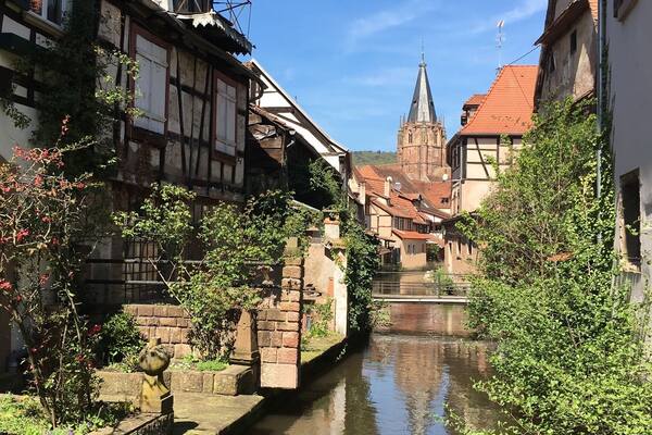 Un étroit canal bordé de maisons traditionnelles à colombages, avec le clocher d’une église en arrière-plan.