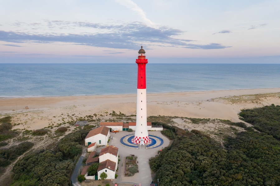 Un paisaje costero con un faro rojo y blanco destacado, una playa de arena y vegetación circundante.