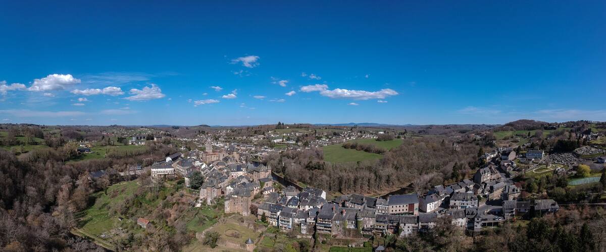 A panoramic view of a town with rolling hills, a mix of residential and historical buildings, and a clear blue sky with scattered clouds.