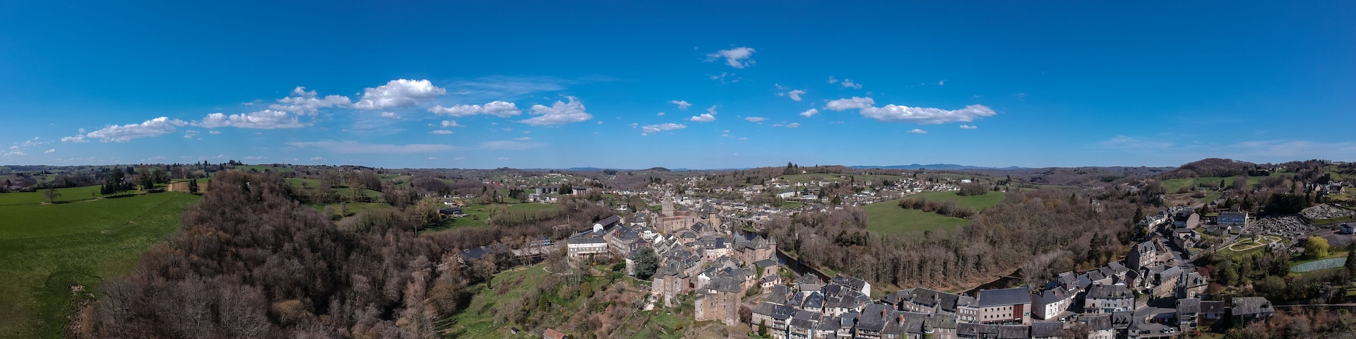 A panoramic view of a town with rolling hills, a mix of residential and historical buildings, and a clear blue sky with scattered clouds.