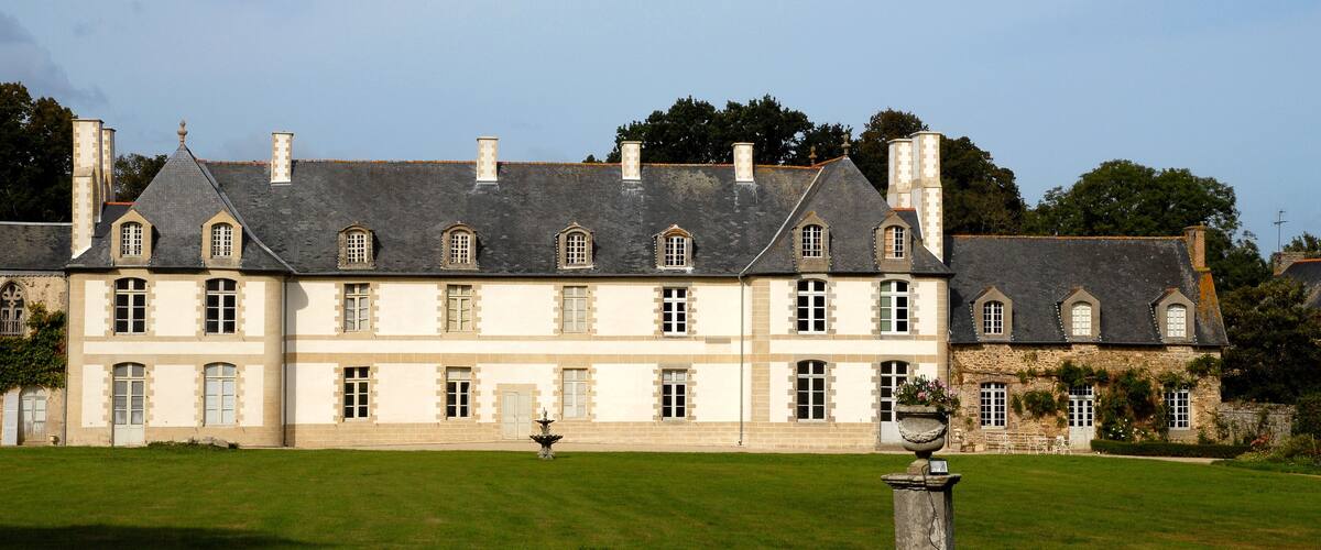 A large, historic building with multiple windows and a well-maintained lawn in front.