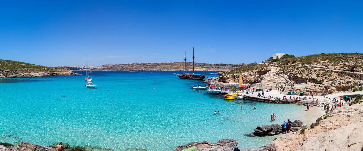 A coastal area with clear turquoise water, rocky terrain, and boats.