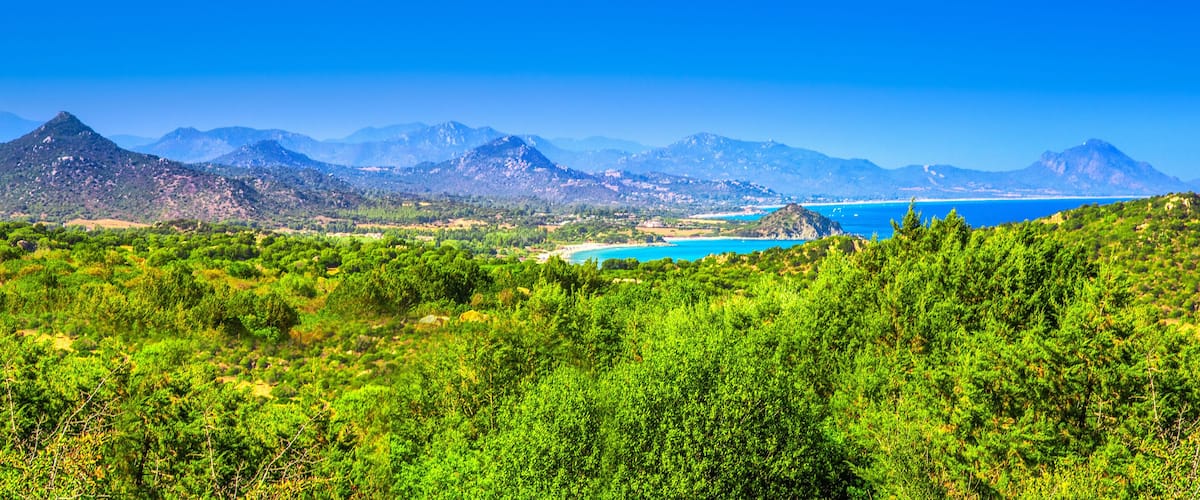 A coastal landscape with green hills, a clear blue sea, and distant mountains.