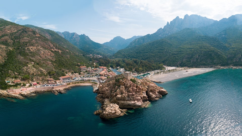 A coastal town with a rocky peninsula, a bay, and mountains in the background.