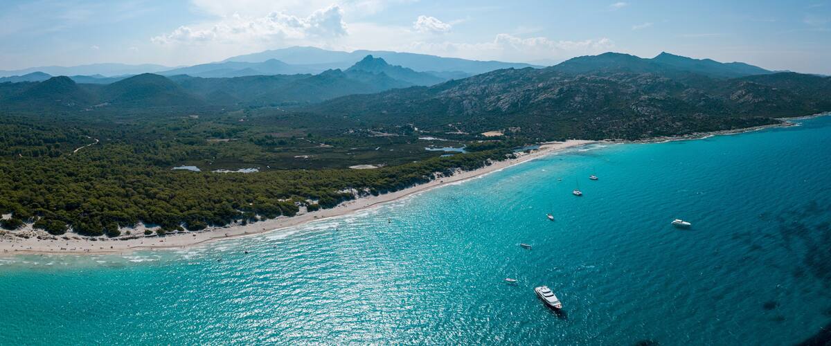 A coastal landscape with turquoise waters, a sandy beach, and a mountainous backdrop.