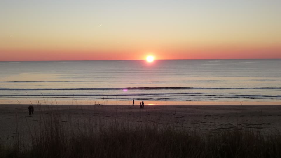 A sunset over a calm sea with a beach in the foreground.