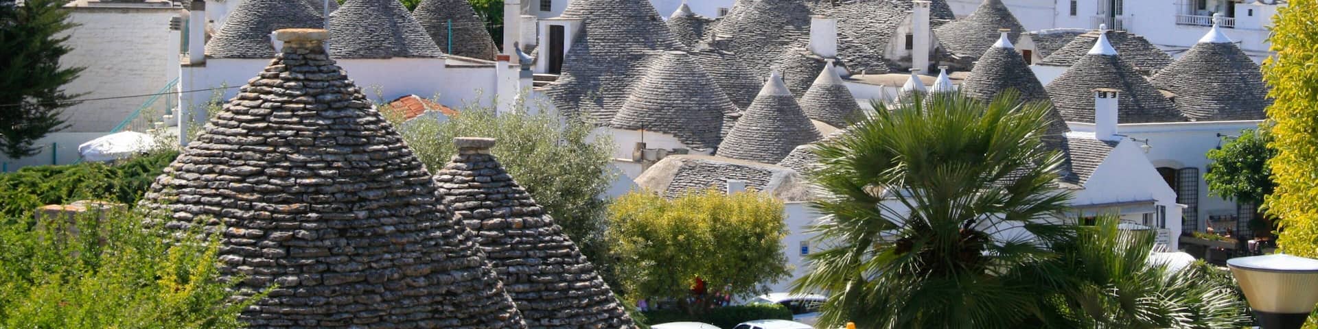 A town with numerous conical-roofed buildings, lush greenery, and a prominent white church.