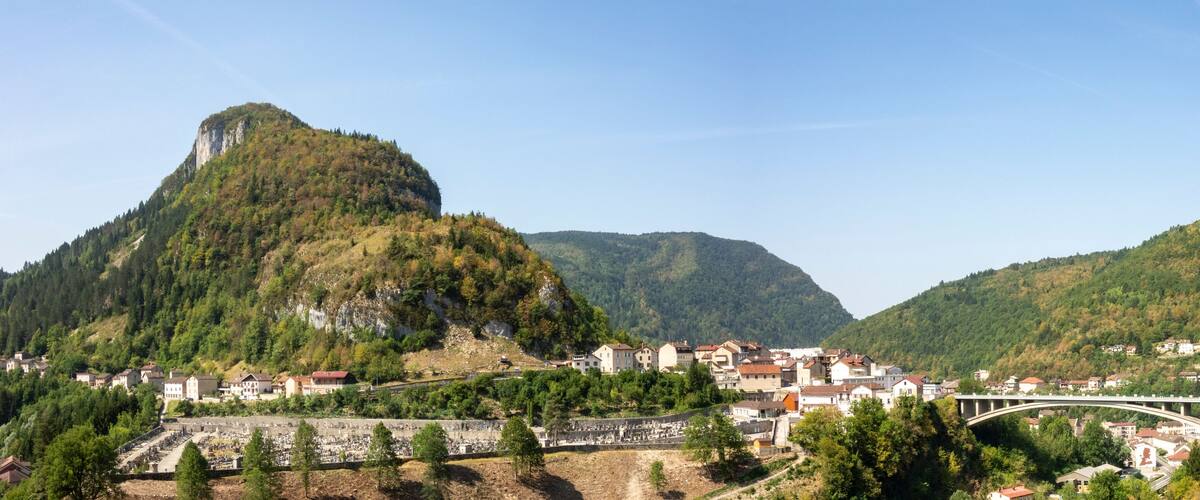 A town nestled between green hills, a prominent mountain, and a bridge.