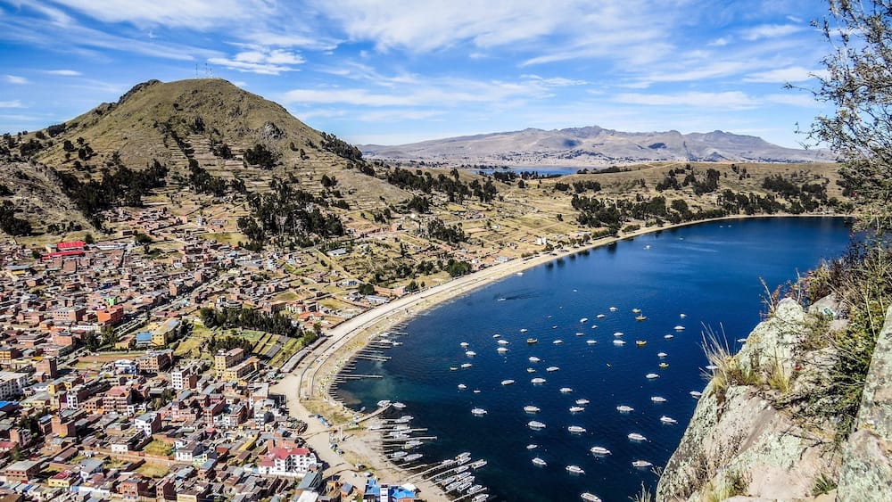 A coastal town with a bay filled with boats, surrounded by hills and sparse vegetation.
