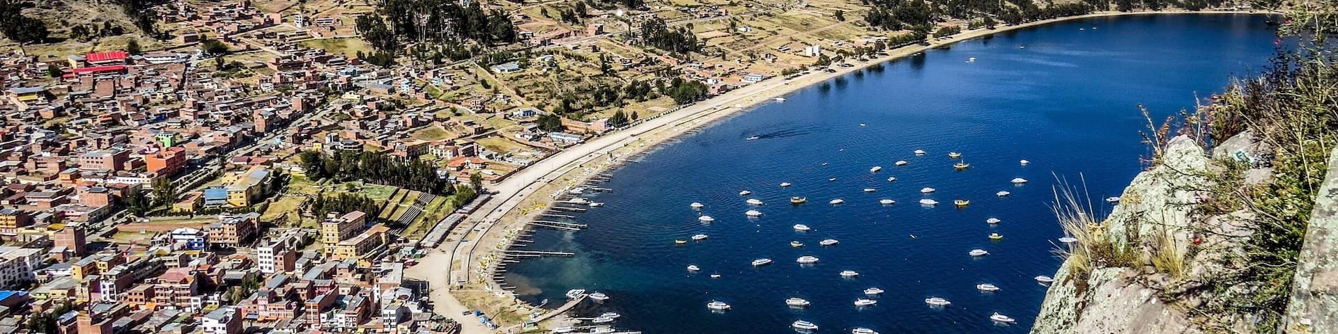 A coastal town with a bay filled with boats, surrounded by hills and sparse vegetation.