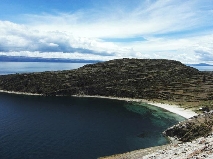 A coastal landscape with terraced fields, a beach, and a body of water.