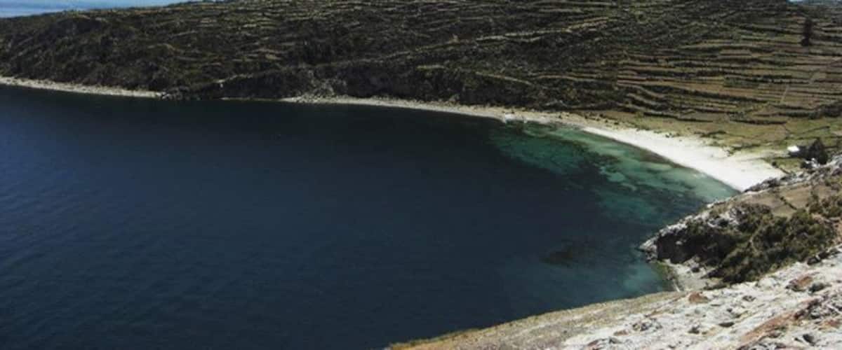 A coastal landscape with terraced fields, a beach, and a body of water.