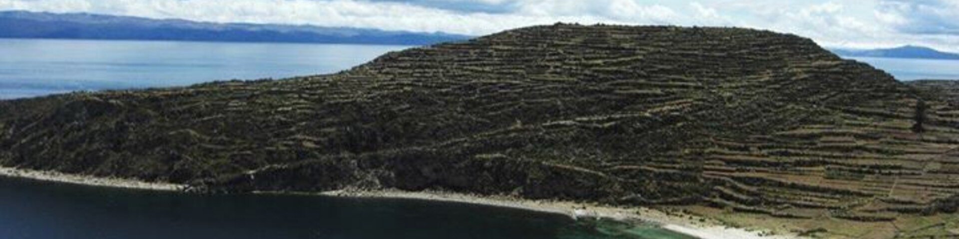 Un paisaje costero con campos en terrazas, una playa y una masa de agua.