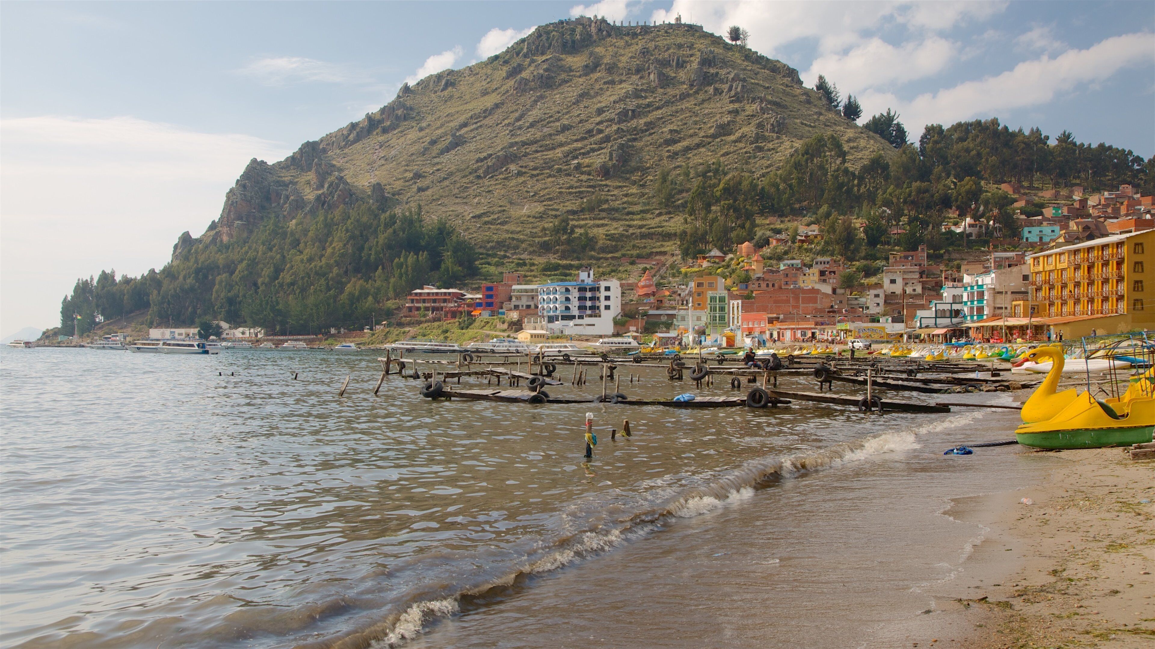 A coastal town with a hill in the background, boats on the water, and colorful buildings along the shore.
