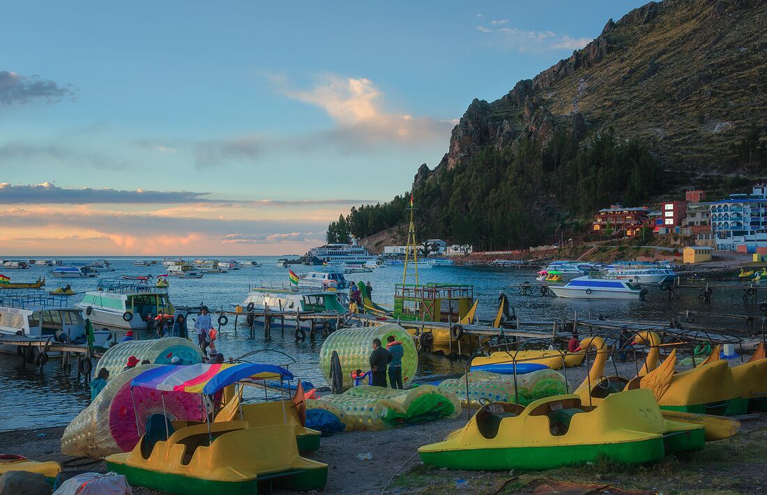 A coastal harbor with colorful boats and a mountainous backdrop.