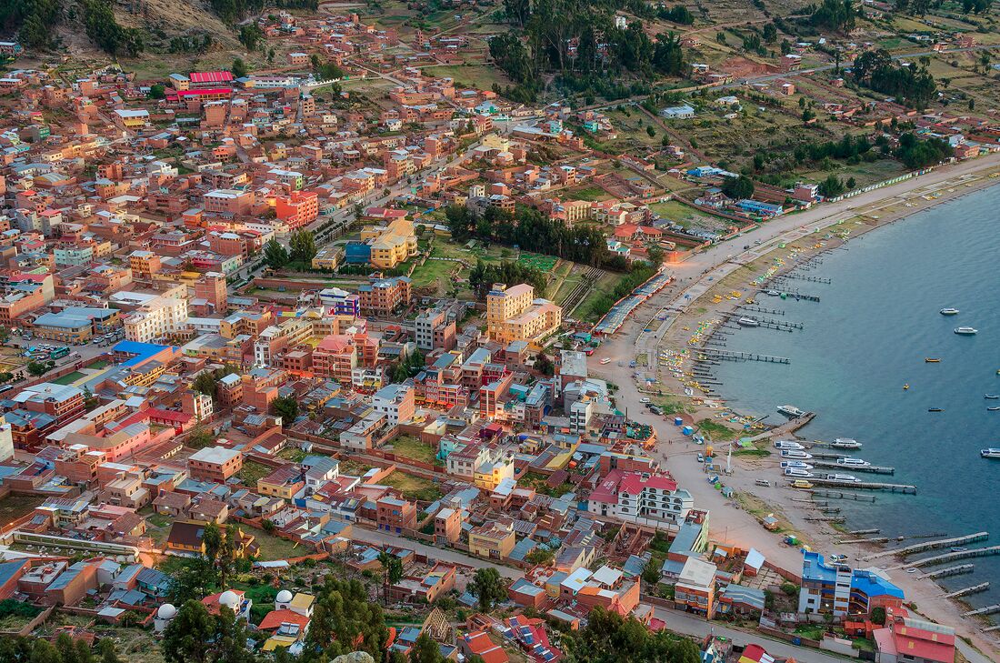 A coastal town with densely packed buildings, a beach, and boats docked along the shore.