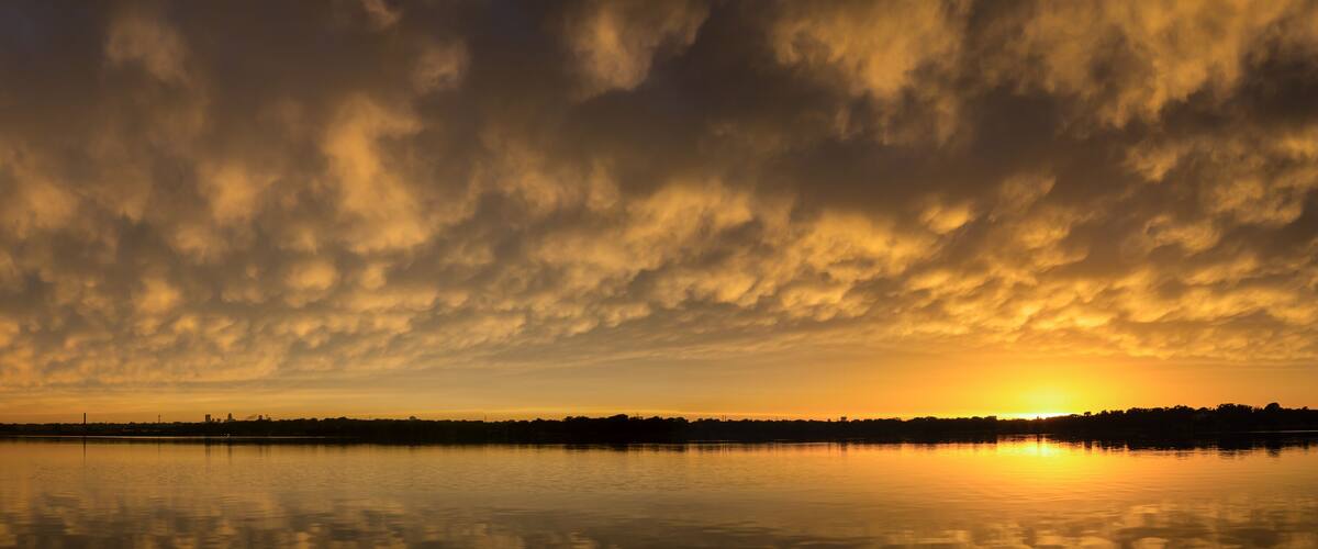 A sunset over a calm lake with a city skyline in silhouette.