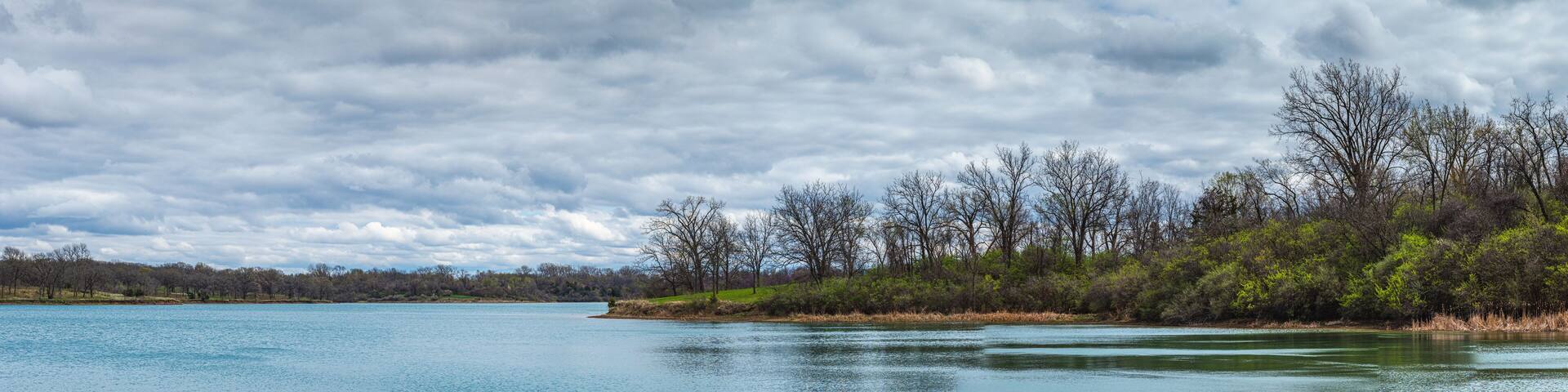 A calm lake surrounded by trees and a cloudy sky.