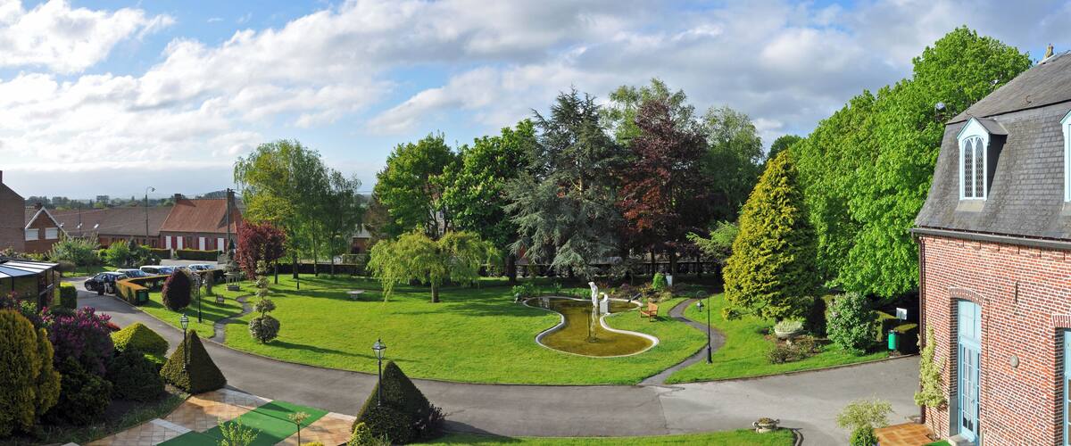 A residential area with a well-maintained lawn, a winding water feature, and a variety of trees.