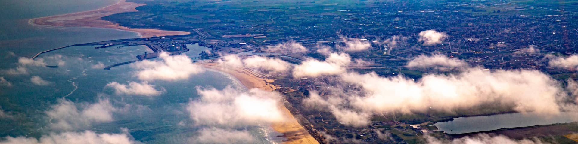 An aerial view of a coastal area with a beach, a river, and surrounding fields.