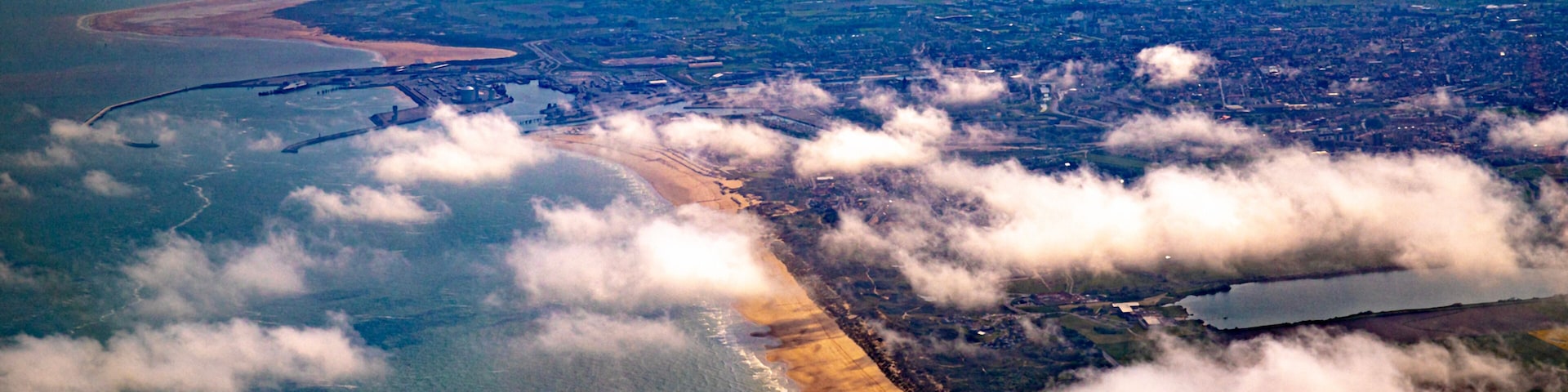 Vista aérea de uma área costeira com praia, rio e campos ao redor.