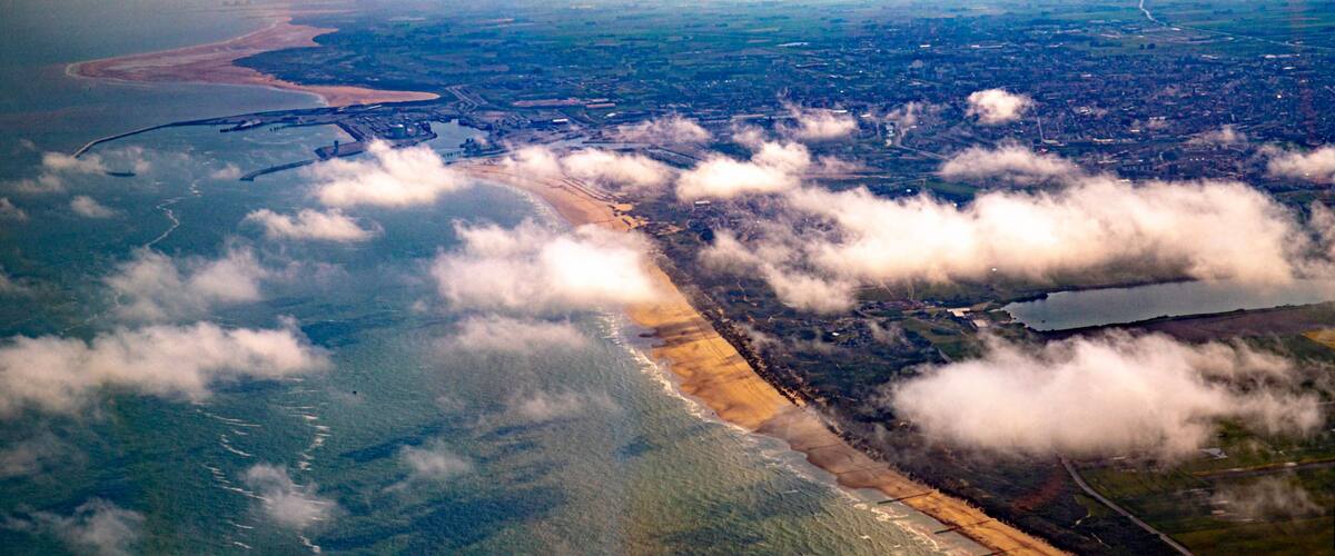 An aerial view of a coastal area with a beach, a river, and surrounding fields.