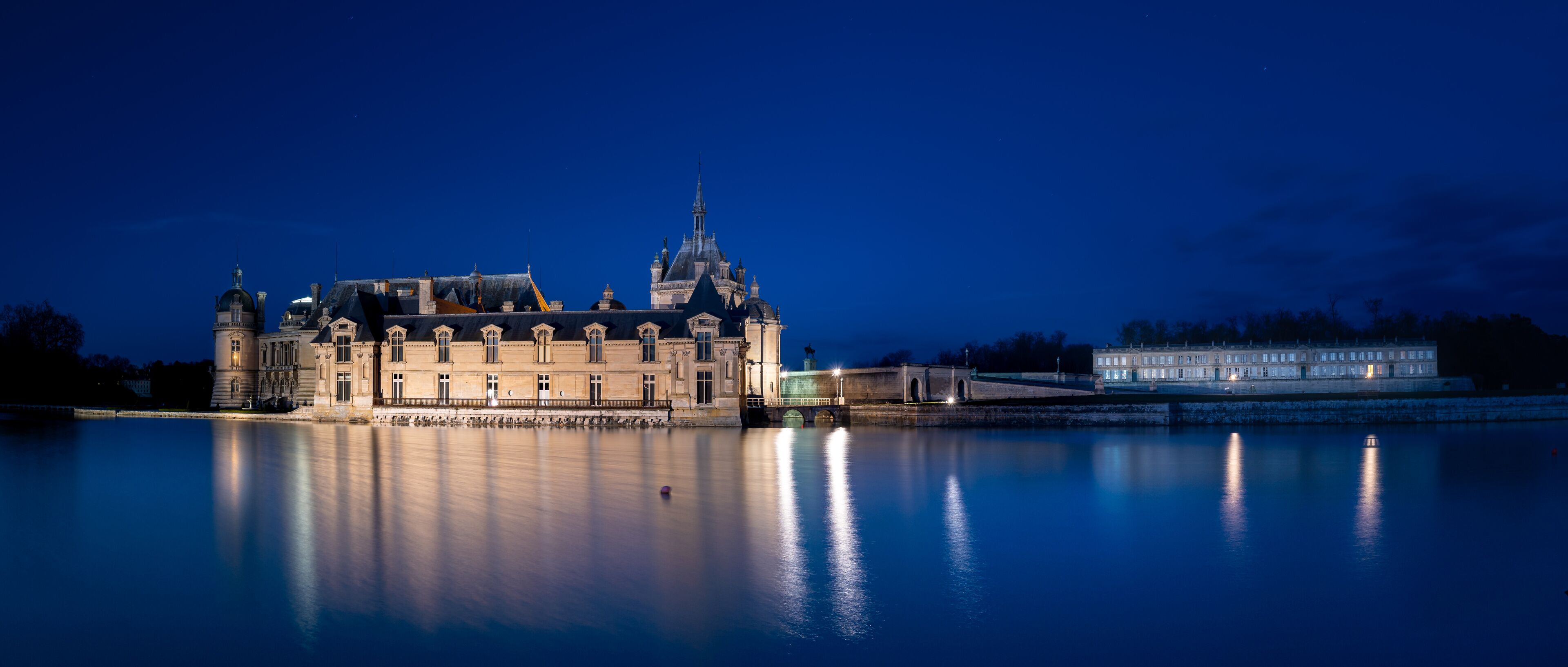 A historic building with a large tower and a bridge over a calm river at night.