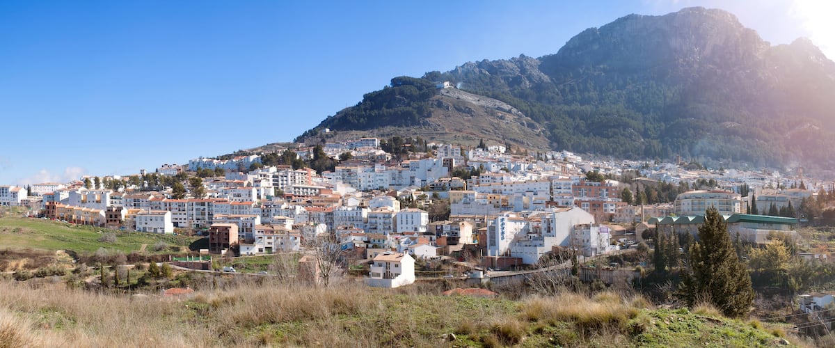 A coastal town with white buildings, a mountain, and a clear sky.