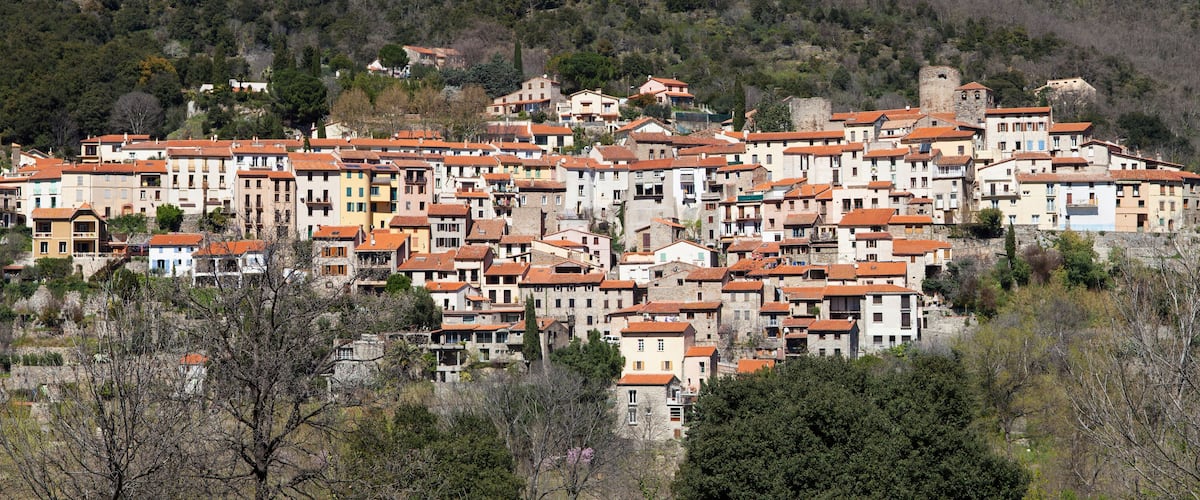 A hillside village with terracotta-roofed buildings and a castle-like structure.