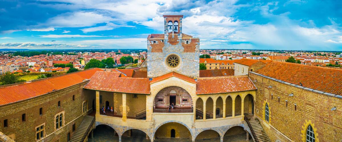 A historic building with a clock tower, arched walkways, and a courtyard.