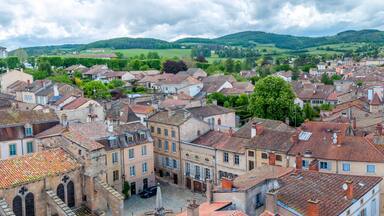A historic town with red-tiled roofs, cobblestone streets, and lush green hills in the background.
