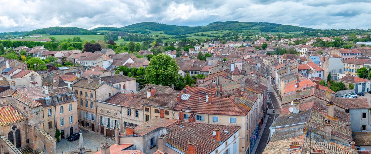 A historic town with red-tiled roofs, cobblestone streets, and lush green hills in the background.