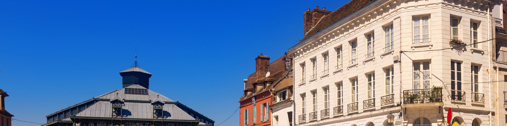 Una plaza histórica de Europa con una torre del reloj distintiva y un edificio blanco con balcones.