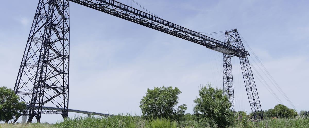 Un gran puente metálico con una estructura de cerchas compleja, rodeado de vegetación y árboles.