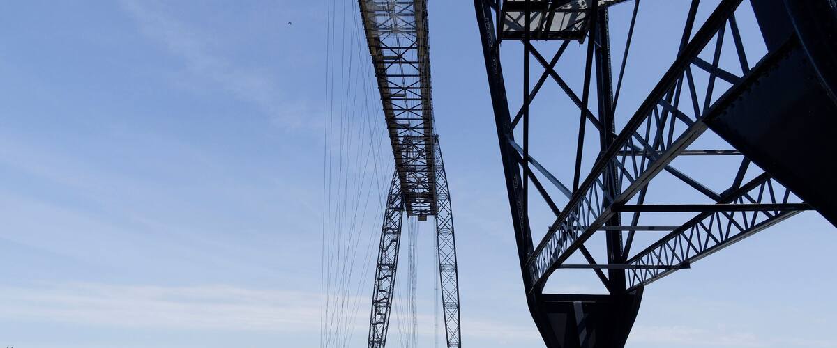 A bridge with a crane and a boat on the water.