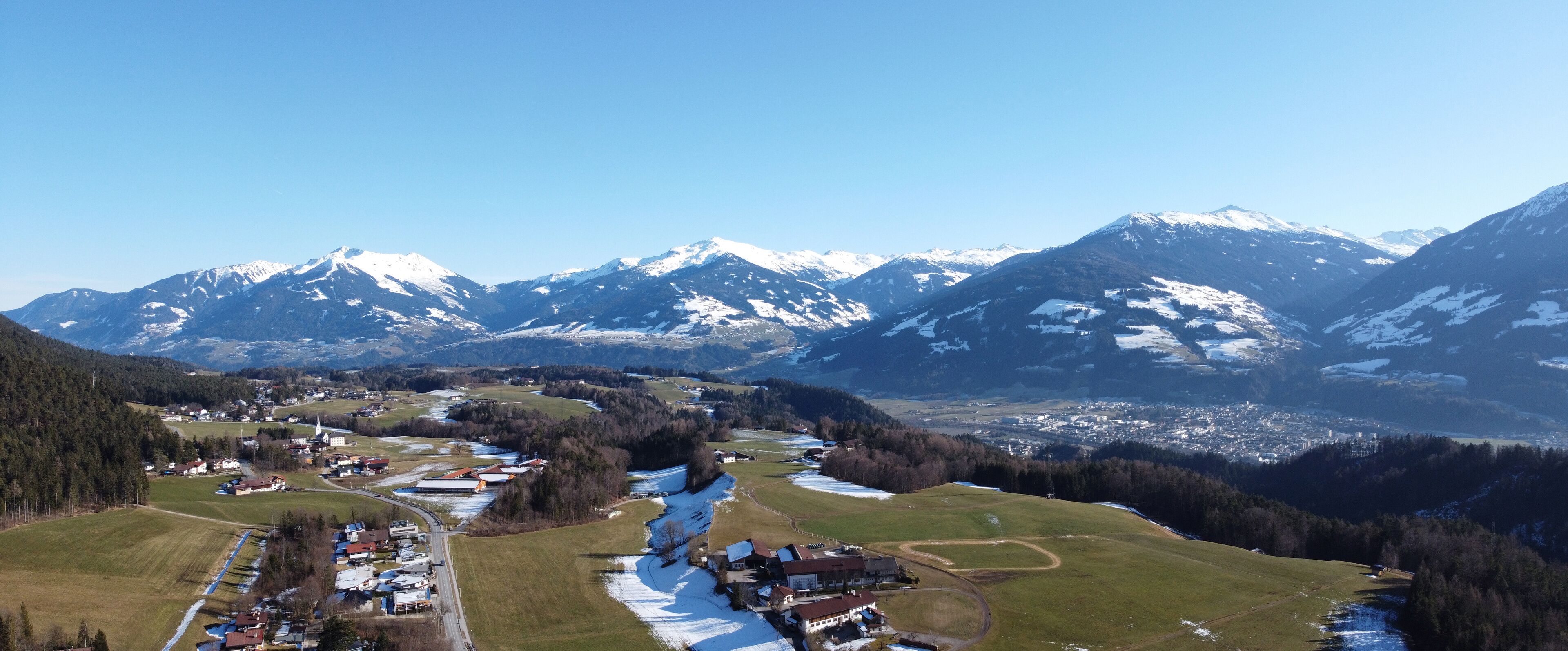 A mountainous landscape with snow-capped peaks, a village with buildings, and a river flowing through the valley.