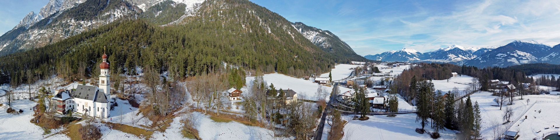 Uma aldeia coberta de neve com uma igreja, casas e montanhas ao fundo.
