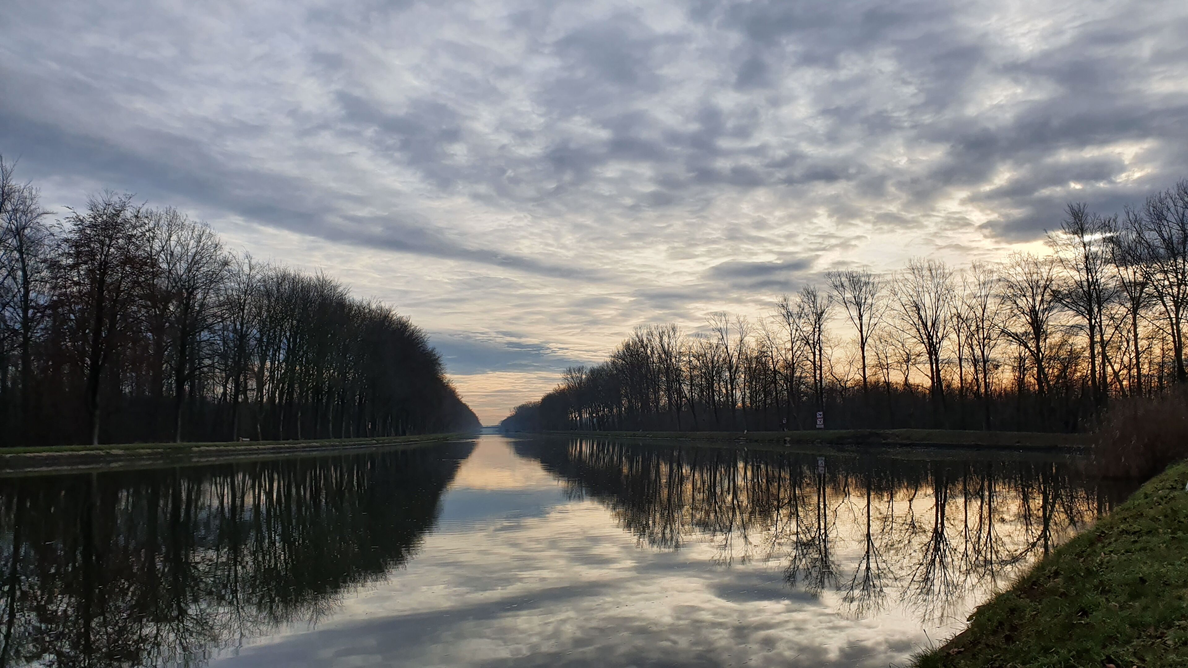 A calm river with reflections of trees and a cloudy sky.
