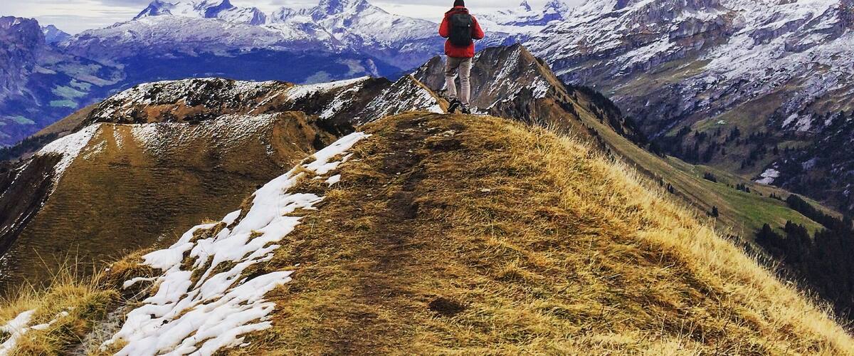 A hiker on a mountain ridge with snow-capped peaks in the background.