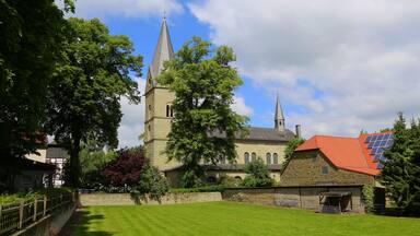 A church with a tall spire, a stone building with a red roof, and a green lawn.