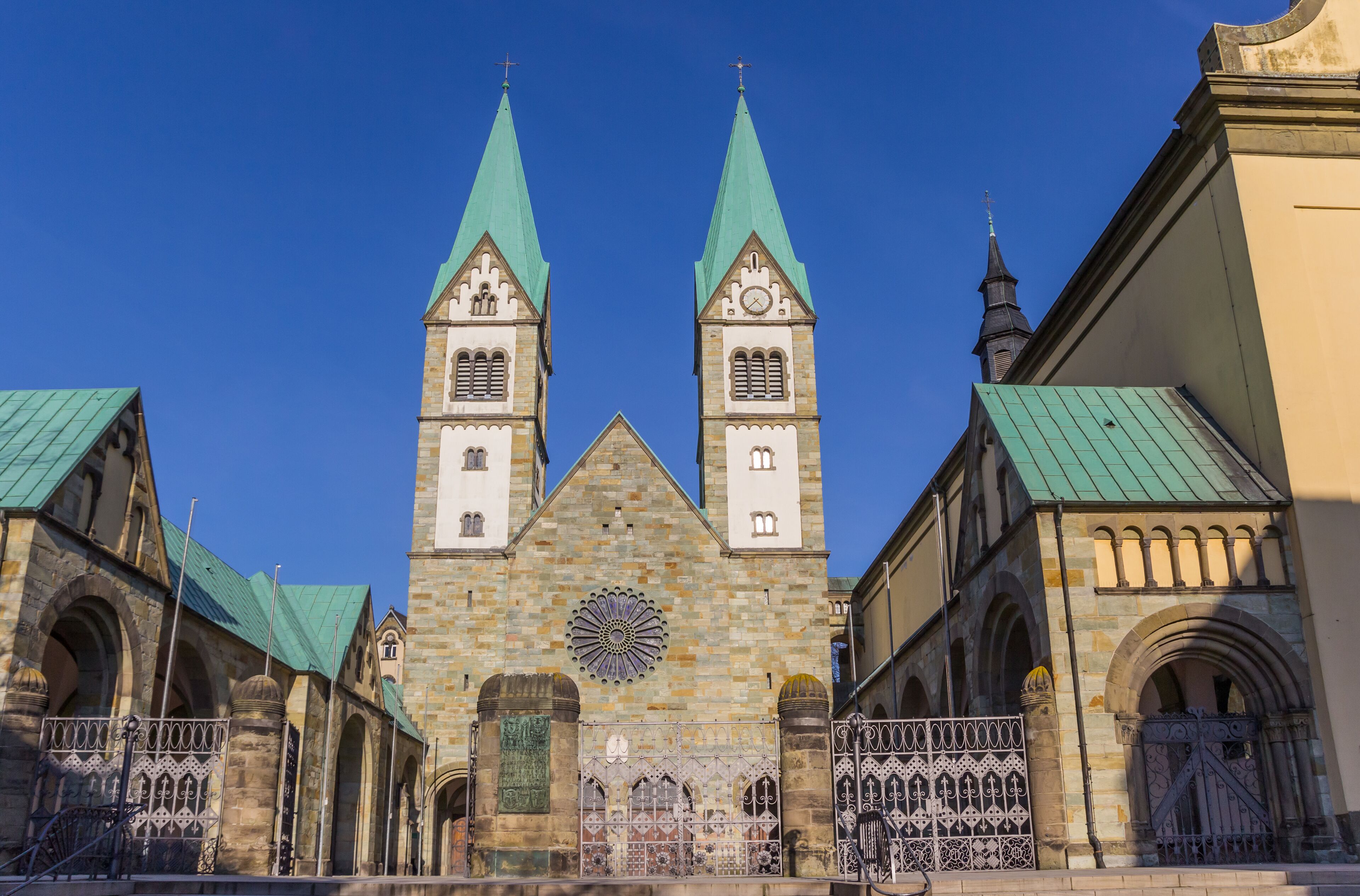 A historic church with two tall spires, a large rose window, and a green roof.
