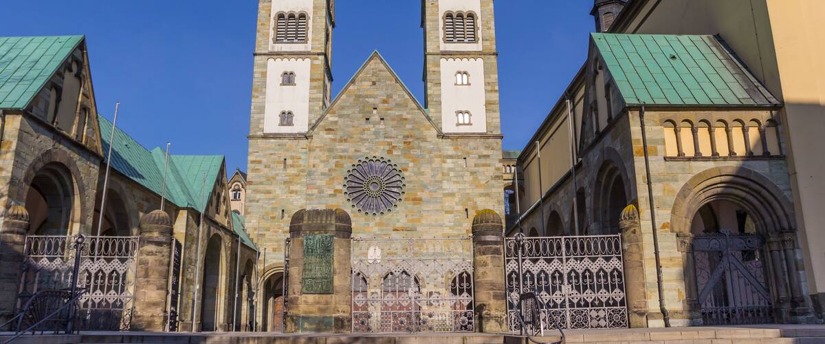 A historic church with two tall spires, a large rose window, and a green roof.