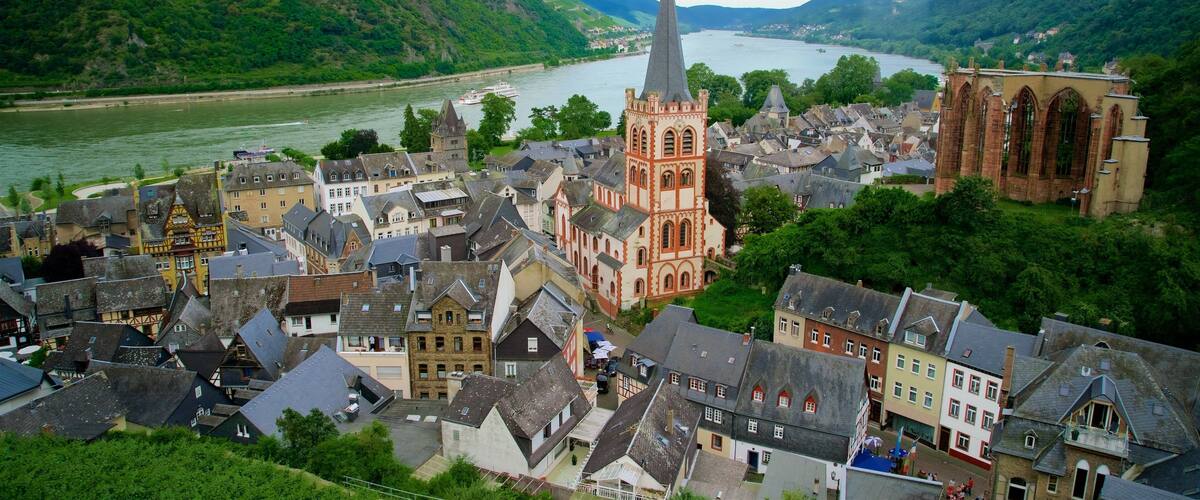 A town with a prominent church tower, a river, and surrounding hills.