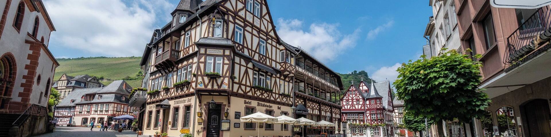 A cobblestone square with traditional half-timbered buildings, outdoor seating, and a sign for 'Jug'.