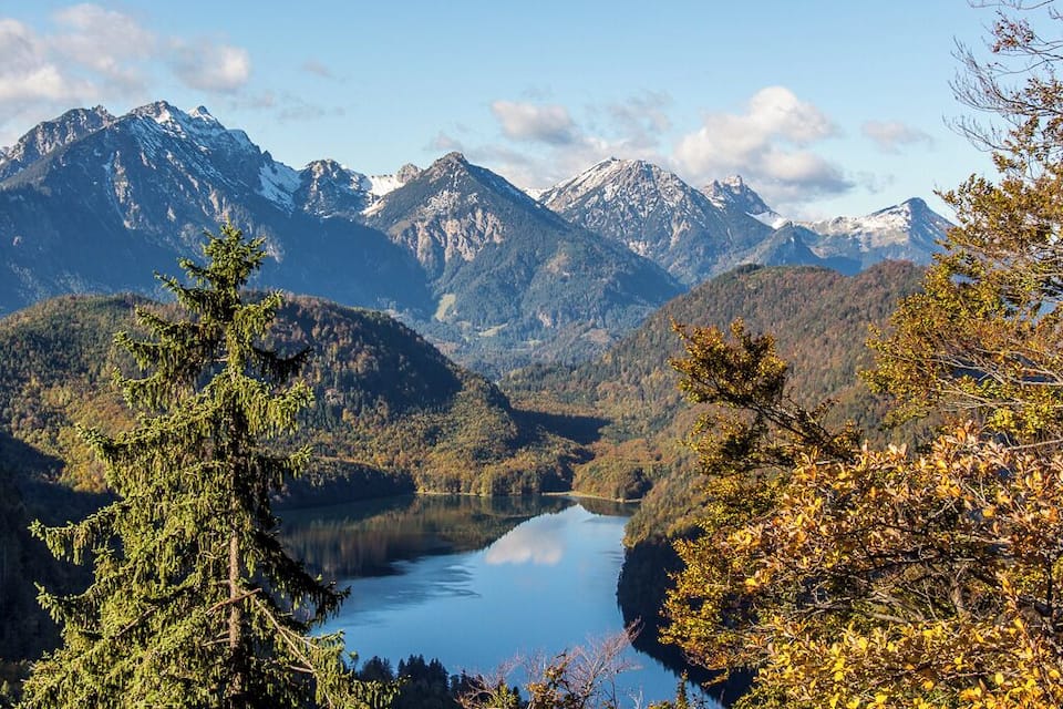 A mountain lake surrounded by forested hills and snow-capped peaks.