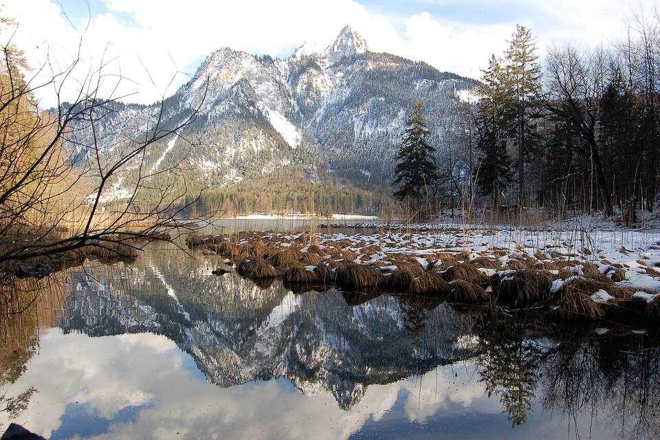A mountain lake with reflections, surrounded by snow-covered trees and mountains.